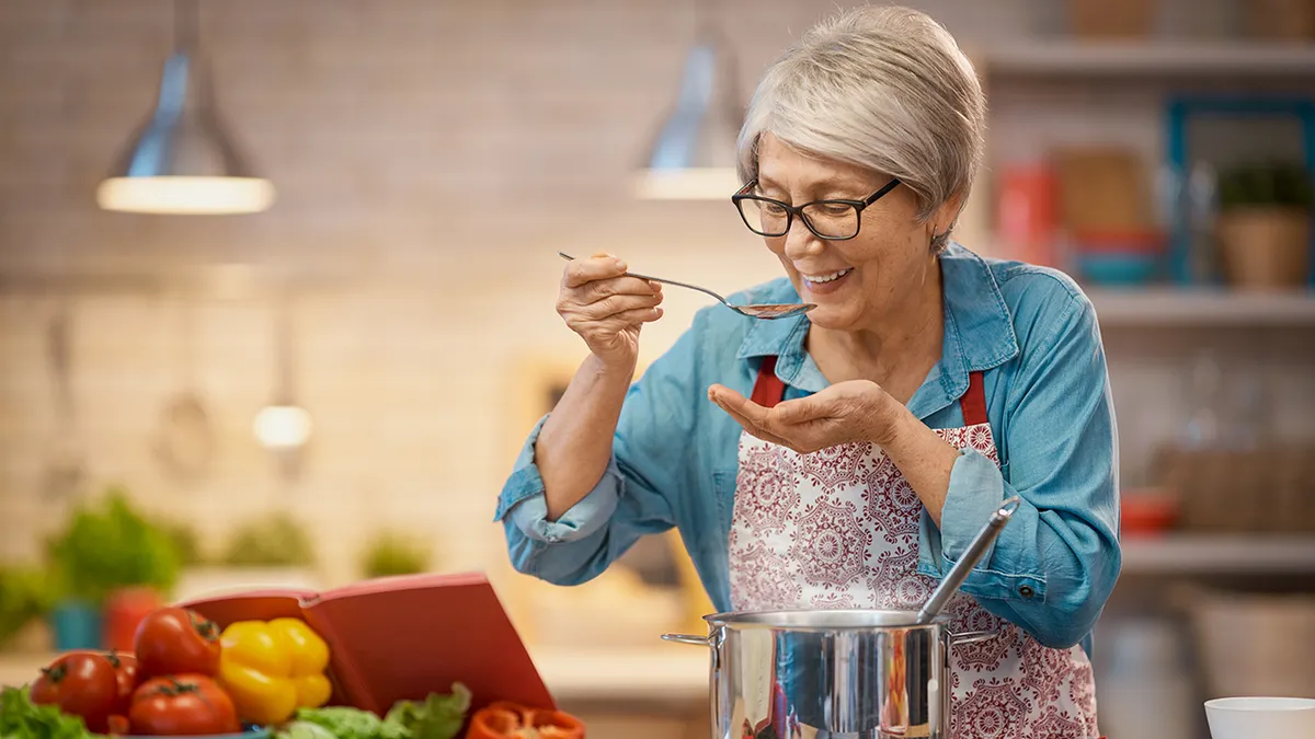Mujer mayor sonriente en su cocina, preparando un remedio casero
